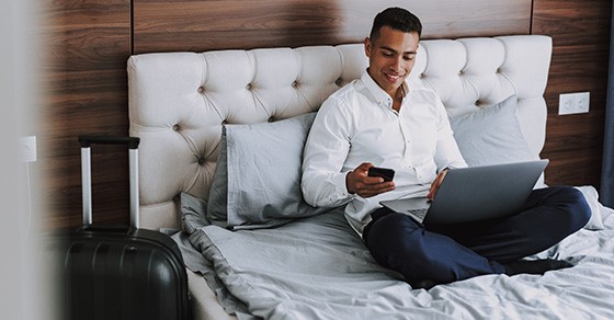 Man looking at phone with laptop on bed